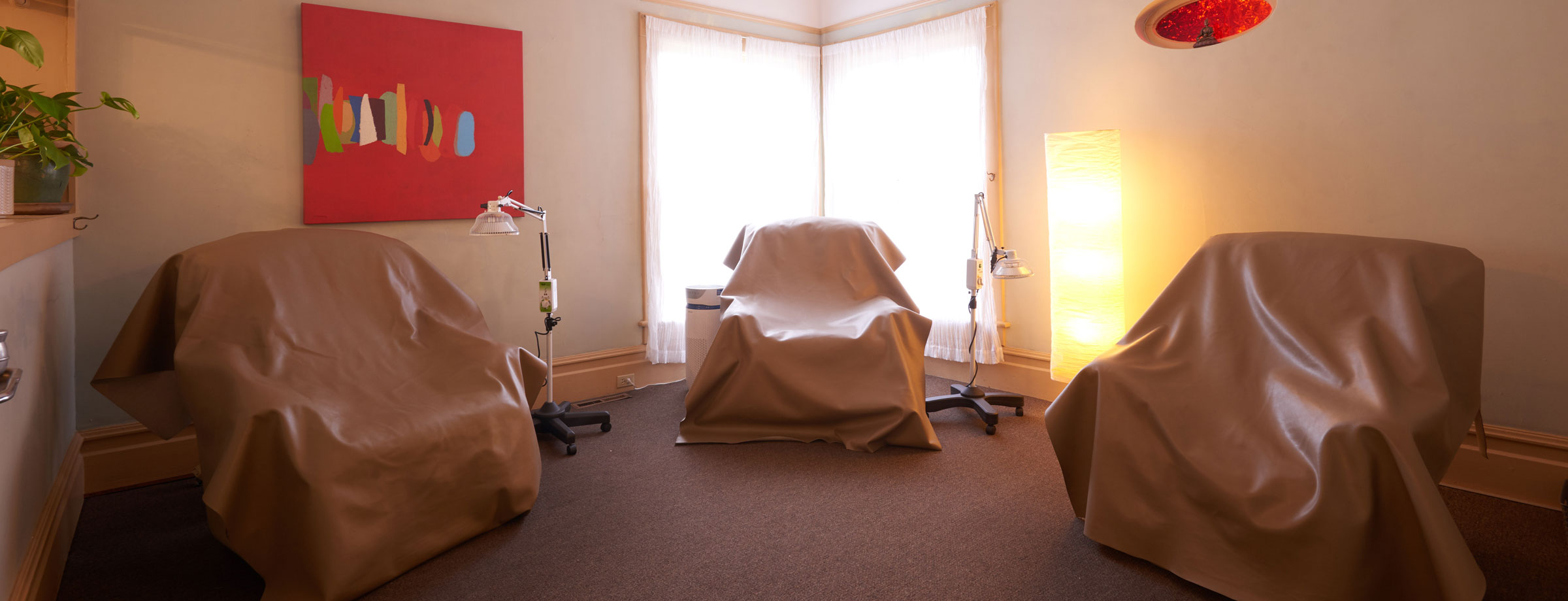 An interior photo showing three chairs, artwork, and lamps at Sebastopol Community Acupuncture